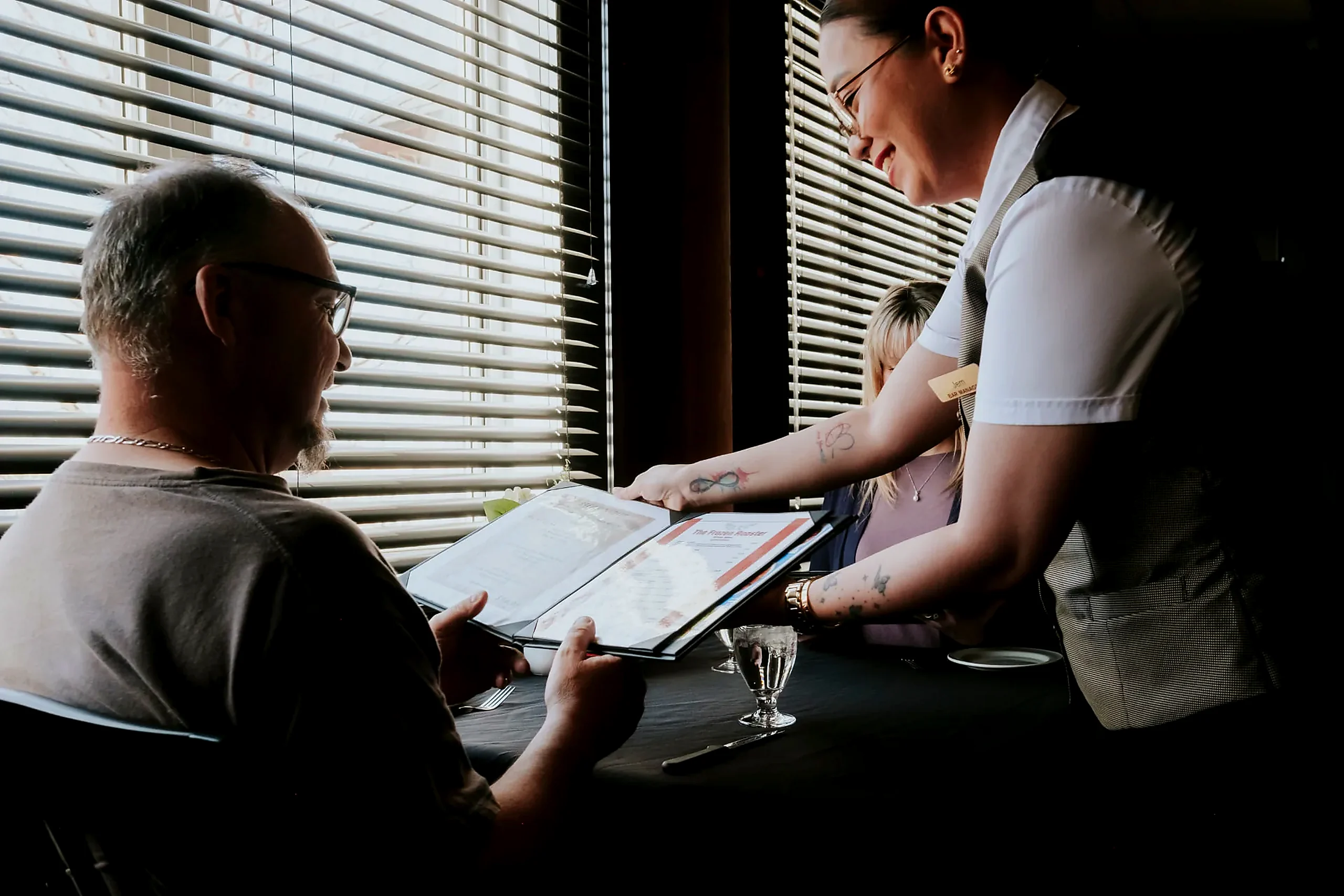 A server presenting the menu to guests at a window table in the restaurant